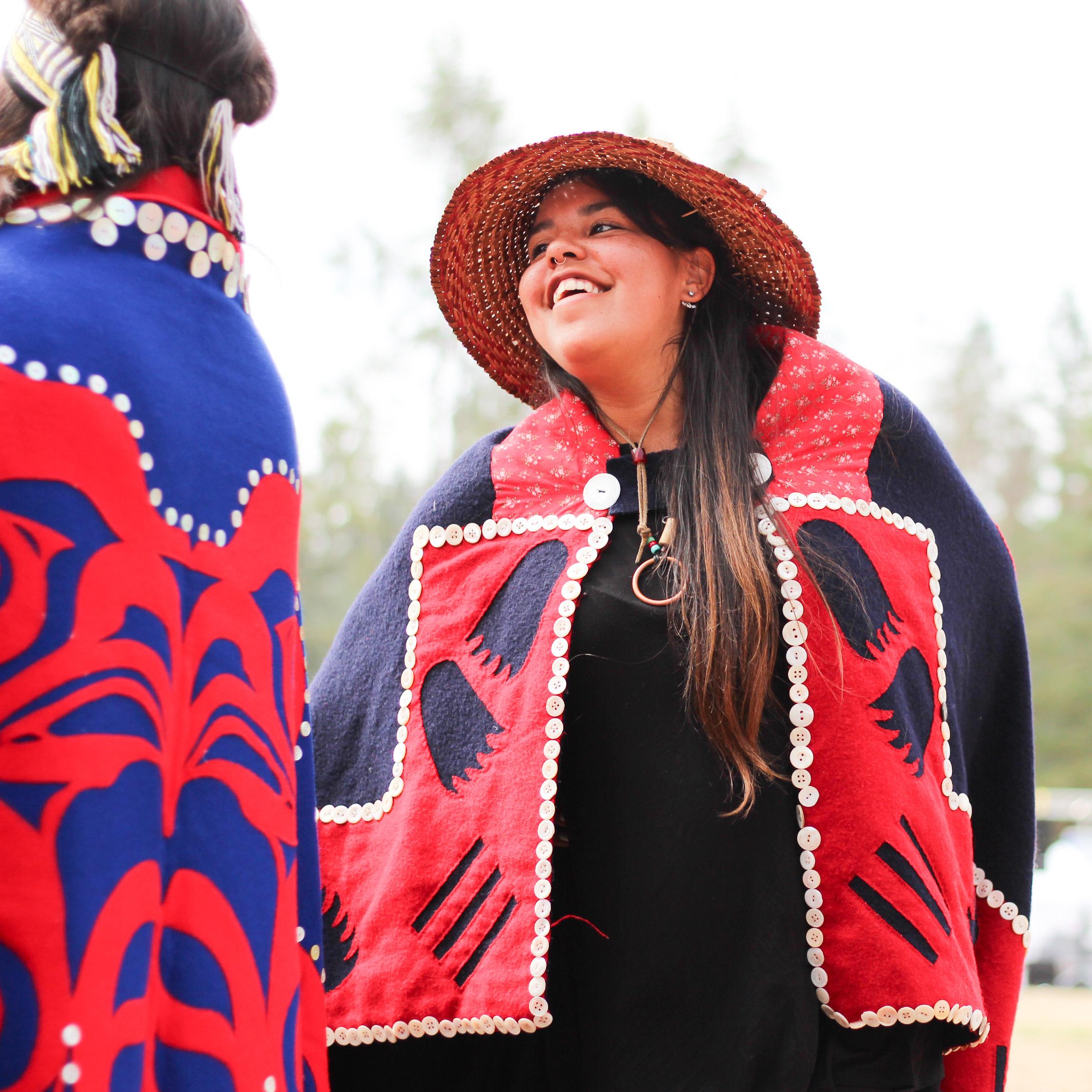 an Indigenous person with long hair smiles while wearing their cultural regalia. - photo by Ricardo Ibarra