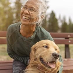 A person with gray hair smiles while embracing her dog.